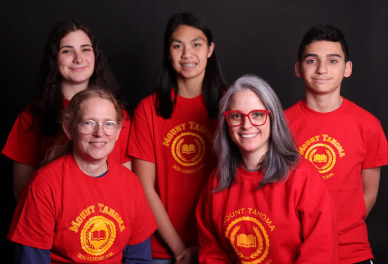 Five individuals are standing together, all wearing bright red t-shirts with a logo that reads 