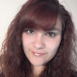 A young person with long, wavy, dark red hair and bangs, smiling softly at the camera against a plain background.