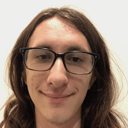 A young person with long, wavy hair and glasses smiles at the camera against a plain white background.