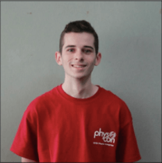 A young man with short brown hair is smiling and wearing a red t-shirt with the word 