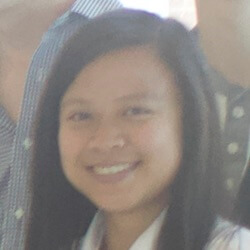 A smiling young person with long black hair, wearing a white shirt, is the focus of the image, with blurred figures in the background.