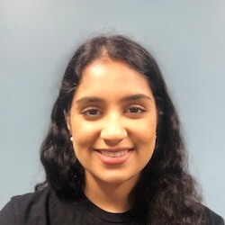 A young woman with long, dark hair and a friendly smile, wearing a black shirt, against a light blue background.