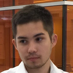 A young man with short hair and a light-colored shirt, looking thoughtfully to the side against a backdrop of warm orange tones.