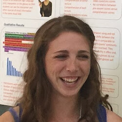 A young woman with curly hair is smiling and laughing in front of a research poster filled with charts and text.