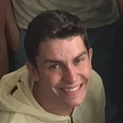 A smiling young man wearing a light-colored hoodie, with short dark hair, positioned in a group setting.