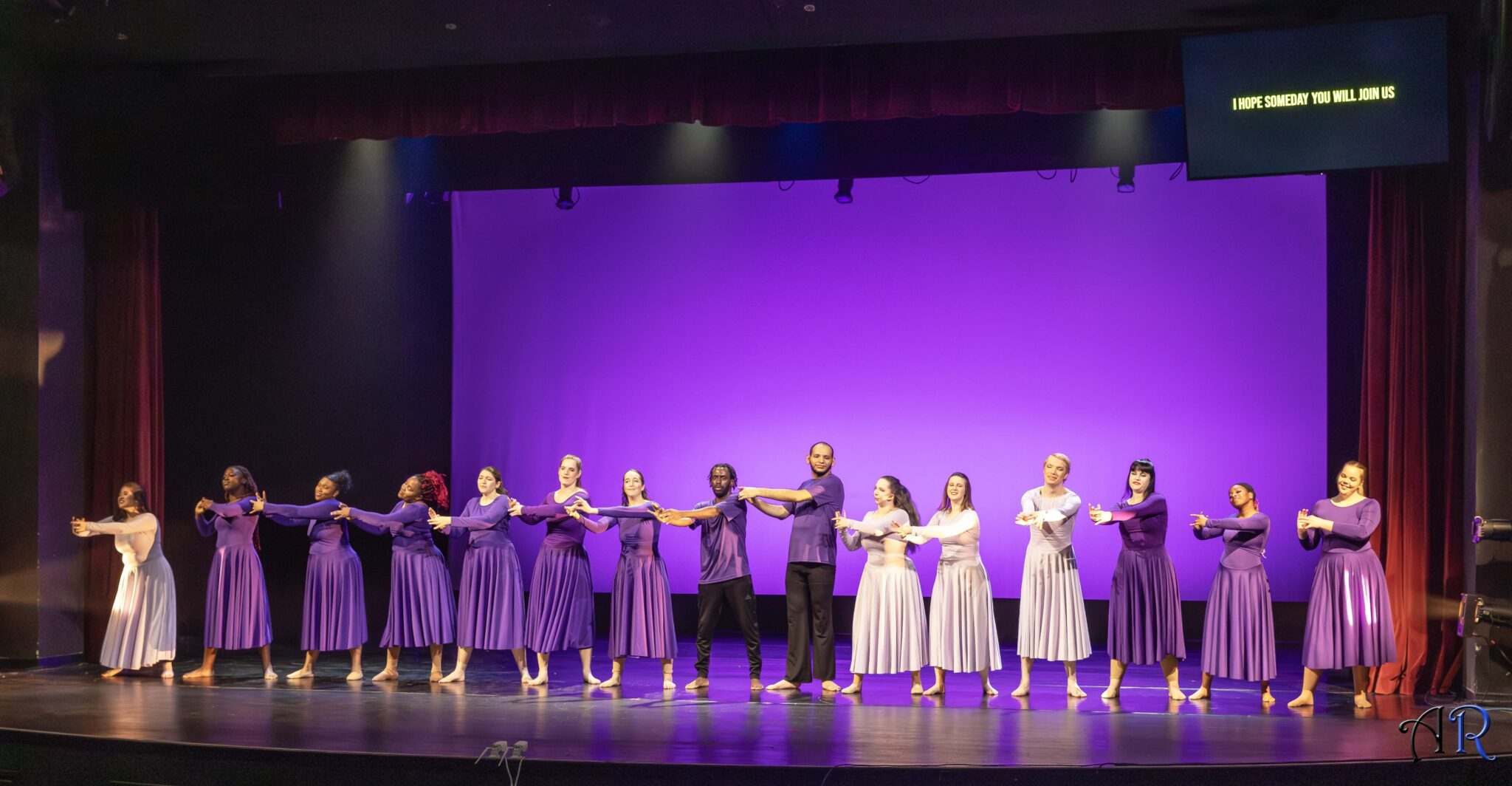 Purple background, line of dancers in front wearing purple dresses, men wearing black pants and purple shirt, all signing “connected” “8-8”