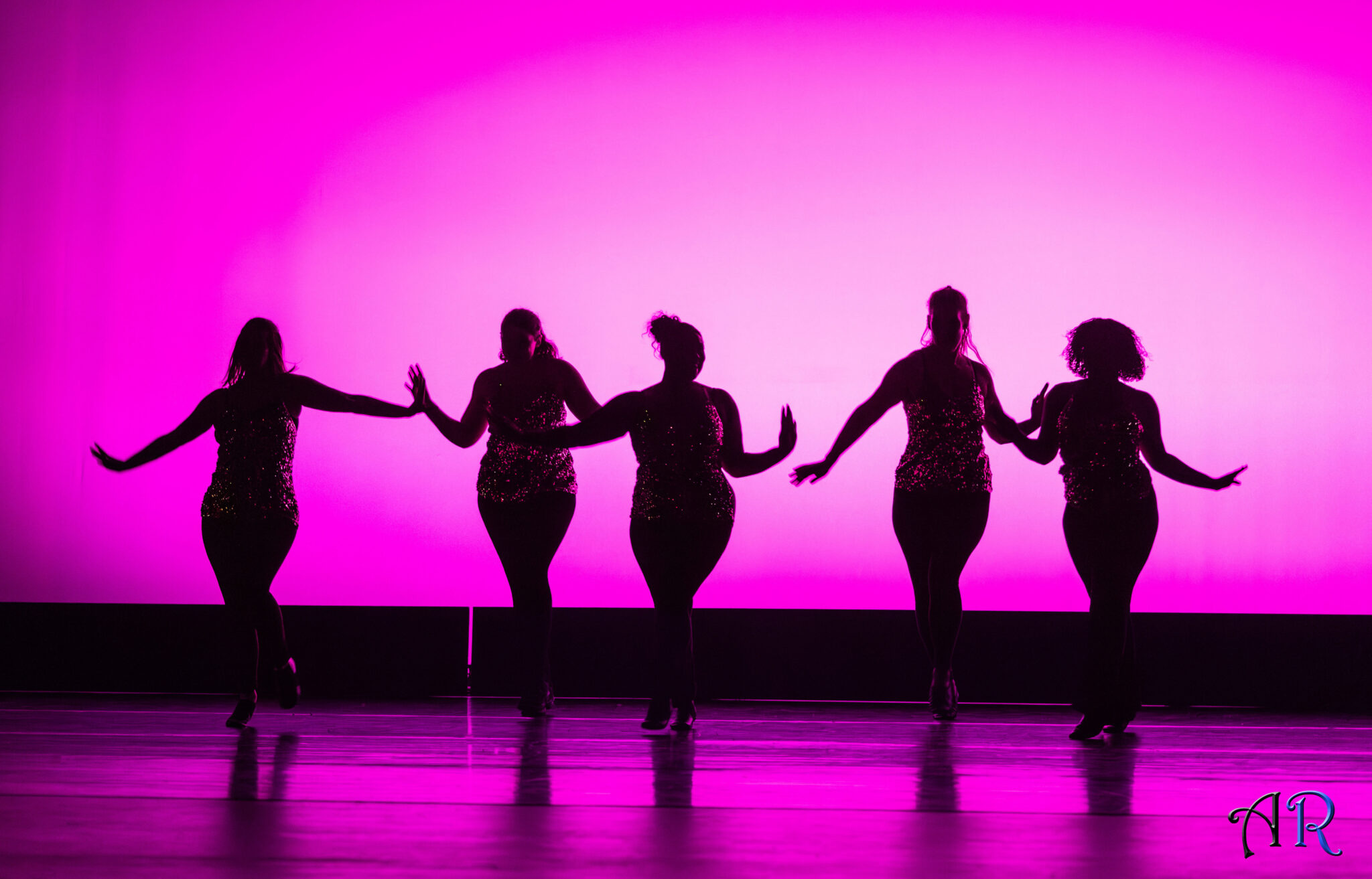Five dancers silhouetted in pink.