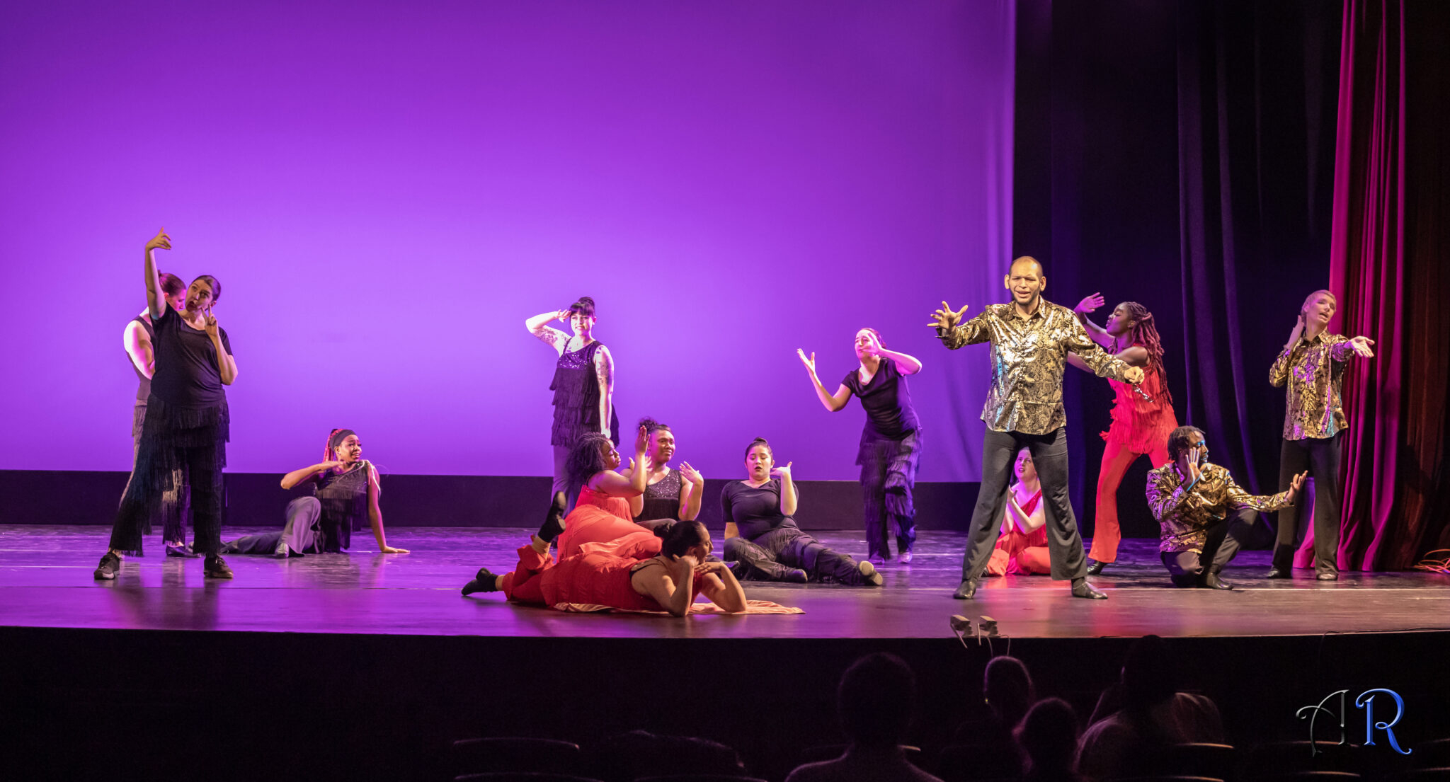 Purple background, women wearing combination of red and black salsa costumes with hanging tassels, 3 men wearing black pants and gold flower print shirt, one men signing in front