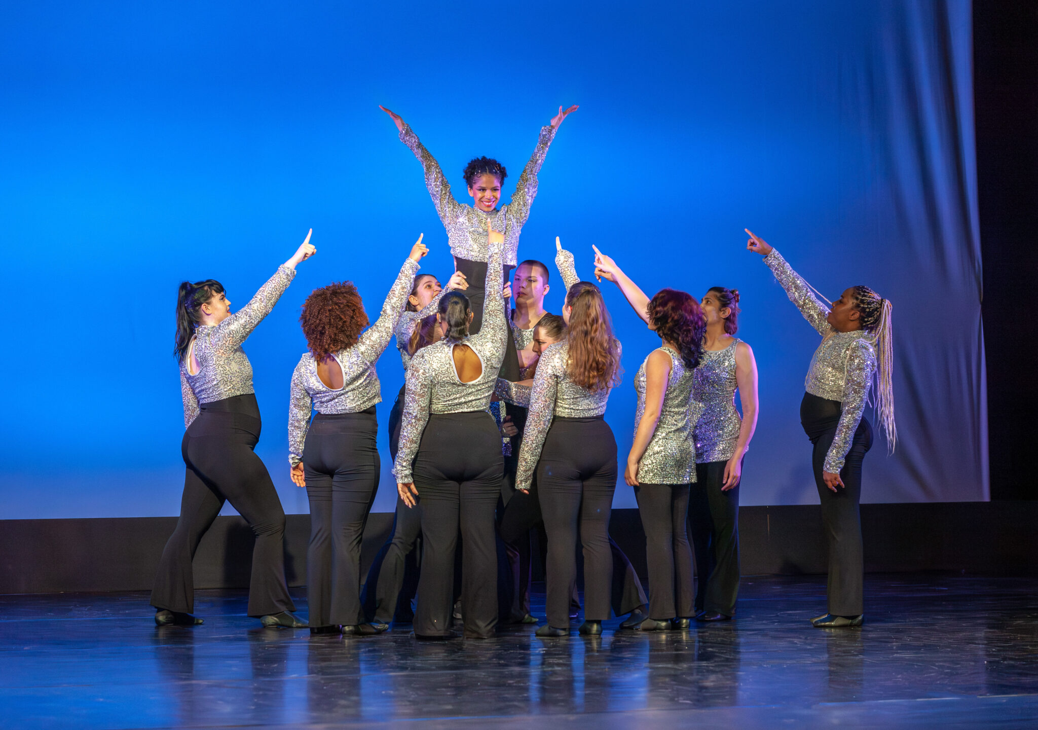 Dancers in black pants, pointing up to a dancer being held up , snake skin leotard