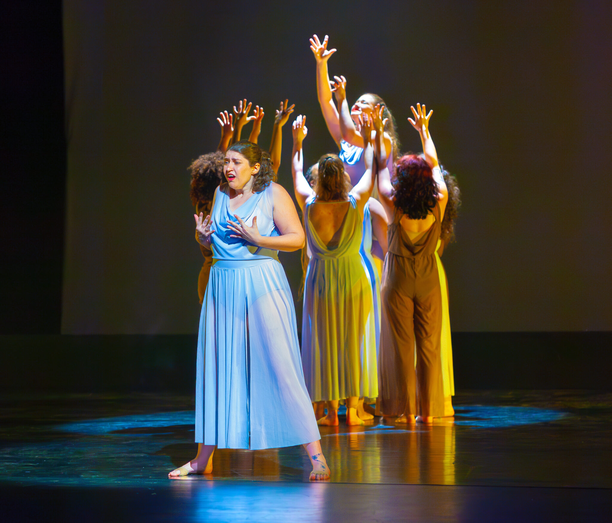 Dancers in blue dress, in circle with their hands up, blue dress singer in the front