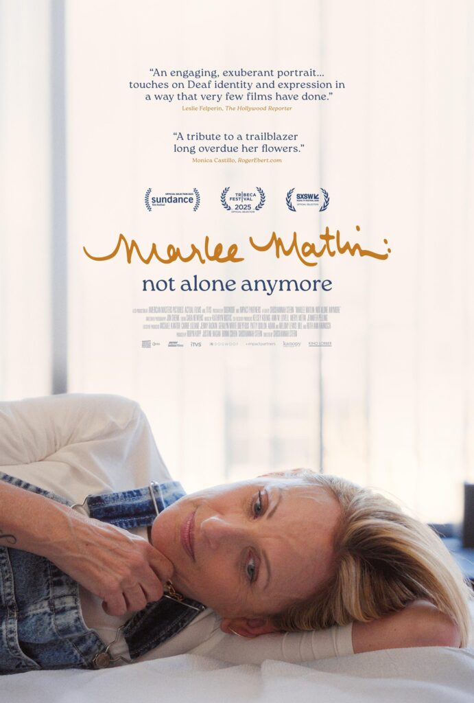 A poster for film Marlee Matlin: Not Alone Anymore. At the bottom, Marlee Matlin is lying down on a bed with white sheets, with the lower half of her body offscreen to the left. She is wearing overalls and a white shirt. Text, from the top of the image to above Marlee's head. "'An engaging, exuberant portrait...touches on Deaf identity and expression in a way that very few films have done.' / Leslie Felperin, The Hollywood Reporter". "'A tribute to a trailblazer long overdue her flowers.' / Monica Castillo, RogerEbert.com". Below the text are laurels from Sundance Film Festival, Tribeca Film Festival, and SXSW. Below the laurels are the film title, then credits in small text.