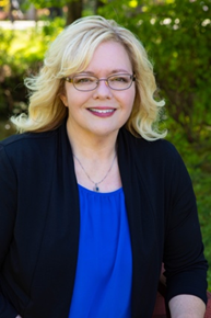 Woman in glasses wears a blue shirt with a black blazer and poses outside