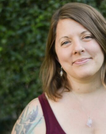 Woman wears a crimson tank top and has a tattoo on her shoulder