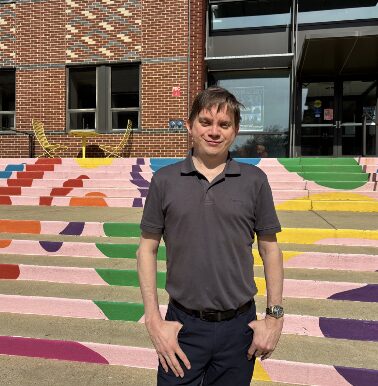 Man in short sleeve collared shirt poses in front of colorful steps