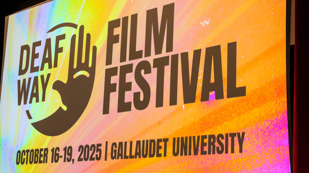 A photo looking up at a projected screen with a colorful orange background. The screen has the Deaf Way logo and text: "Film Festival / October 16-19 / Gallaudet University".
