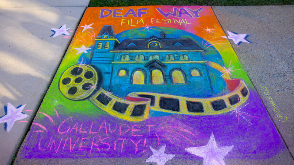 A photo of chalk art on a sidewalk. It is a colorful representation of a building with a movie reel around it. On the top and bottom it says "Deaf Way Film Festival / Gallaudet University".