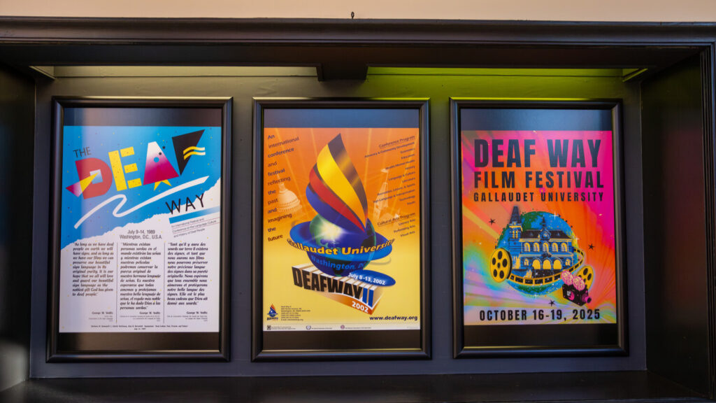 A photo of three framed posters. On the left is a poster with 80s-style branding that says "The Deaf Way". In the middle is a poster with early-internet branding that says "Gallaudet University / Deaf Way II / 2002". On the right is a colorful poster with more modern branding that says "Deaf Way Film Festival / Gallaudet University / October 16-19, 2025".
