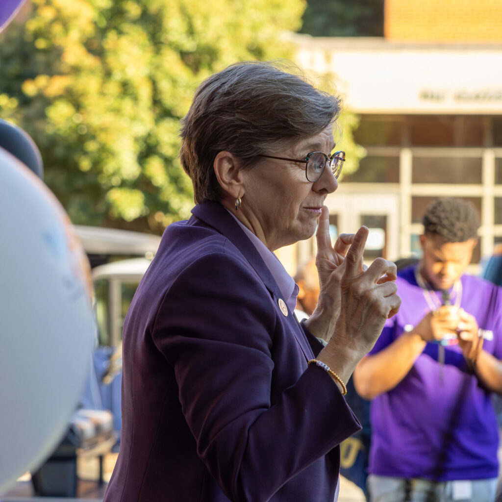 A photo of Gallaudet President Roberta Cordano signing outdoors toward an unseen audience to the right.