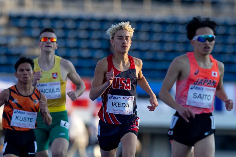 A photo of four runners in mid-stride. The runner prominent in the center is wearing a dark blue and red uniform reading "USA". They look focused as they try to catch up to an out-of-focus runner in the foreground with a "Japan" uniform.
