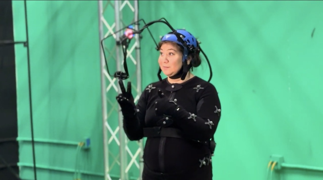 Woman dressed in all black and wearing a helmet with a camera attached is in an all-green room.