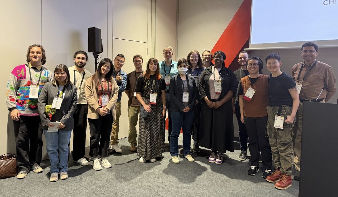 Large group of people stand in the corner of a room.