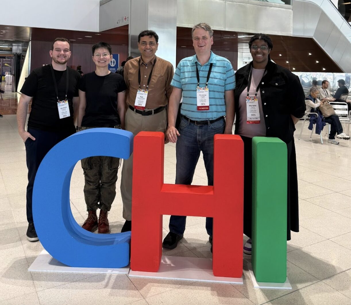 Five people wearing lanyards stand in front of large letters: a blue "C," a red "H," and a green, "I."