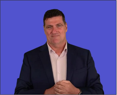Headshot of Brett Casey, standing against a bright blue background, wearing a navy blue blazer over a white button down shirt.